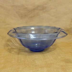 May include: A blue glass bowl with a wavy rim. The bowl is sitting on a brown burlap surface.