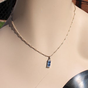 May include: A silver chain necklace with a small rectangular pendant featuring a blue gemstone.