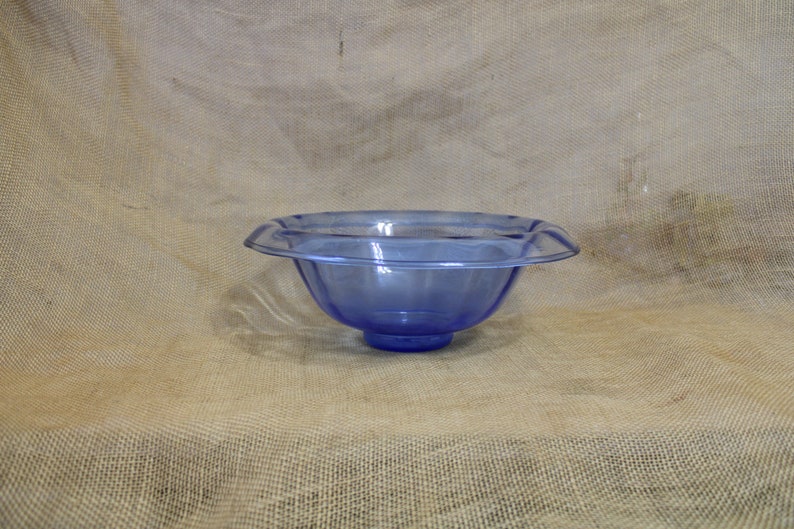 May include: A large, clear blue glass bowl with a scalloped rim. The bowl is sitting on a burlap background.