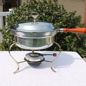 May include: A silver chafing dish with a wooden handle and a gold stand. The chafing dish has a lid with a decorative knob.