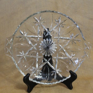 May include: A clear glass serving dish with a scalloped edge and a starburst pattern. The dish has two handles on the sides.