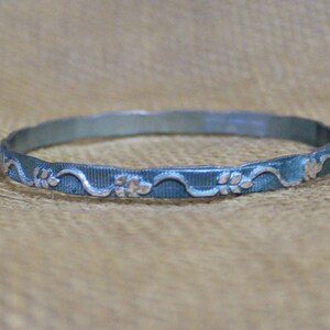 May include: A silver bangle bracelet with a blue patina and a floral design.