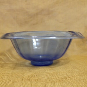 May include: A blue glass bowl with a wide rim and a rounded base. The bowl is clear and has a slight blue tint.