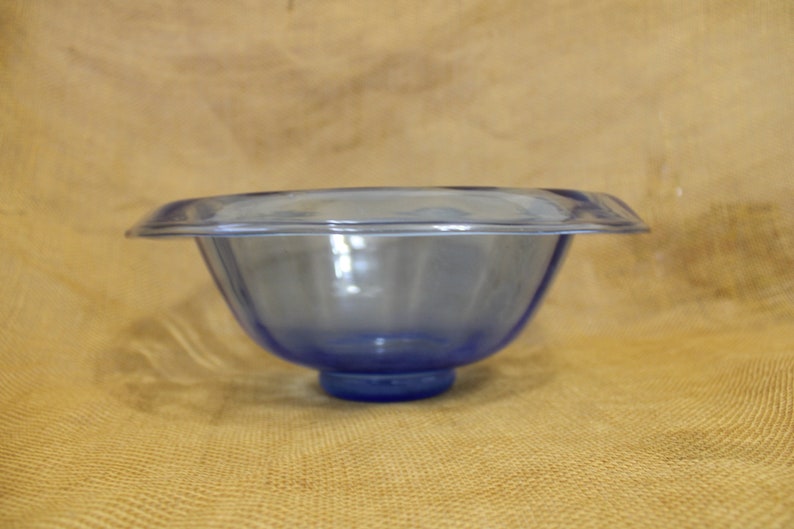 May include: A blue glass bowl with a wide rim and a rounded base. The bowl is clear and has a slight blue tint.