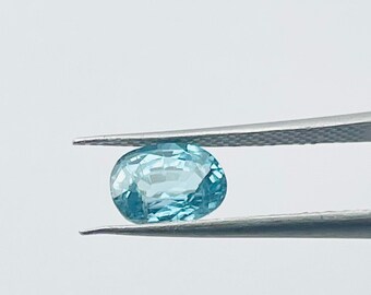 May include: A light blue oval-shaped gemstone held by tweezers against a white background.