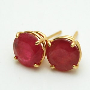 May include: A pair of gold earrings with red gemstone studs. The earrings are shown with their backs.