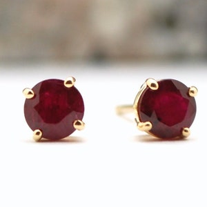 May include: A pair of gold stud earrings with round red ruby gemstones.
