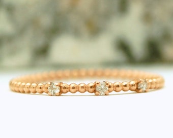 May include: A delicate rose gold ring featuring a beaded band design. The ring is adorned with four small, sparkling diamonds evenly spaced along the band. The ring is a minimalist piece of jewelry.