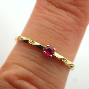May include: A gold ring featuring a delicate, swirling design and a single, bright red gemstone.