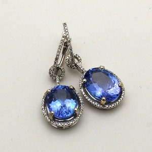 May include: A pair of dangle earrings with oval-shaped blue gemstones surrounded by a halo of small diamonds. The earrings are made of silver and have a drop design.