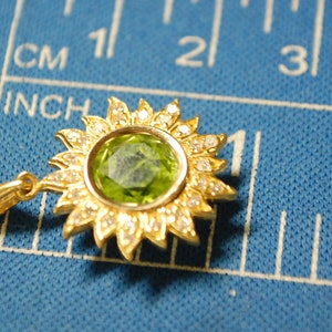 May include: A gold pendant in the shape of a sun with a green gemstone in the center and small white stones around the edge.