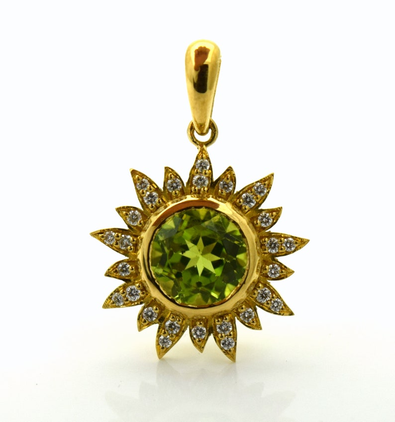 May include: A gold pendant featuring a green gemstone surrounded by a halo of small diamonds. The pendant is shaped like a sun with rays.