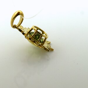 May include: A gold pendant with a green gemstone set in a delicate, ornate design. The pendant has a loop for attaching to a chain.