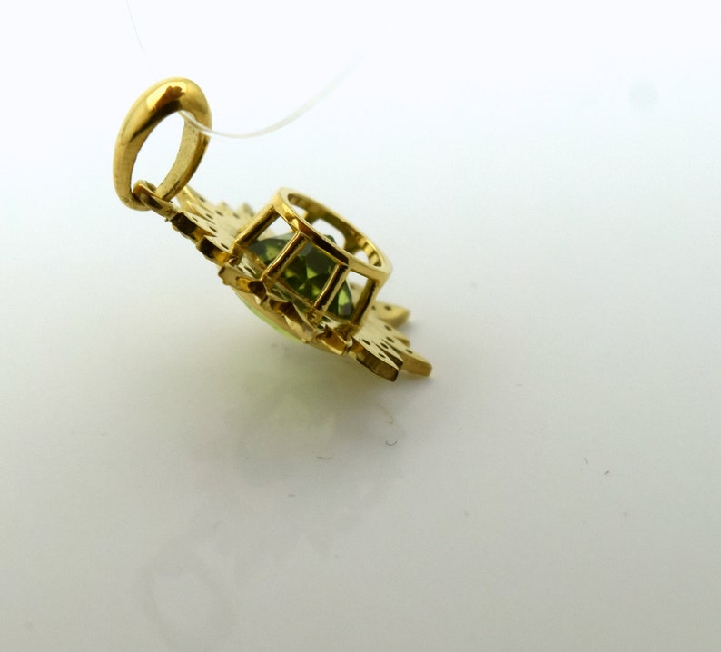 May include: A gold pendant with a green gemstone set in a delicate, ornate design. The pendant has a loop for attaching to a chain.