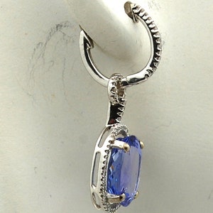 May include: A silver hoop earring with a dangling oval-shaped blue gemstone surrounded by a halo of smaller white gemstones.