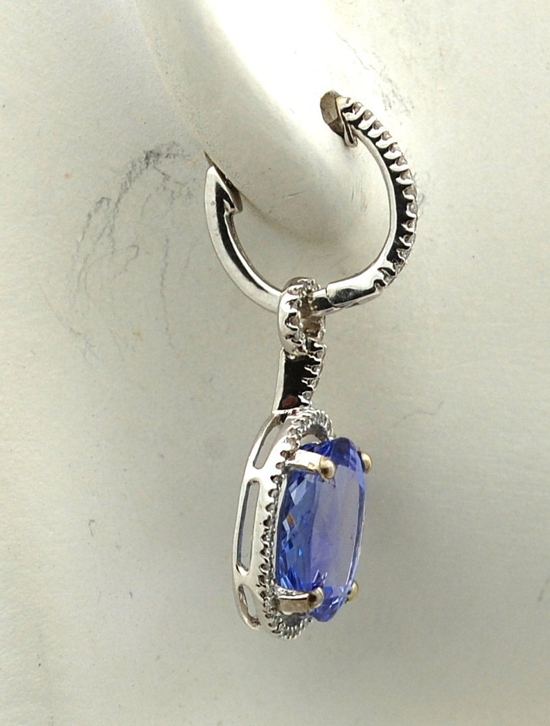 May include: A silver hoop earring with a dangling oval-shaped blue gemstone surrounded by a halo of smaller white gemstones.