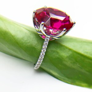 May include: A silver ring with a large, oval-shaped ruby gemstone set in a prong setting. The ring has a band of small diamonds.