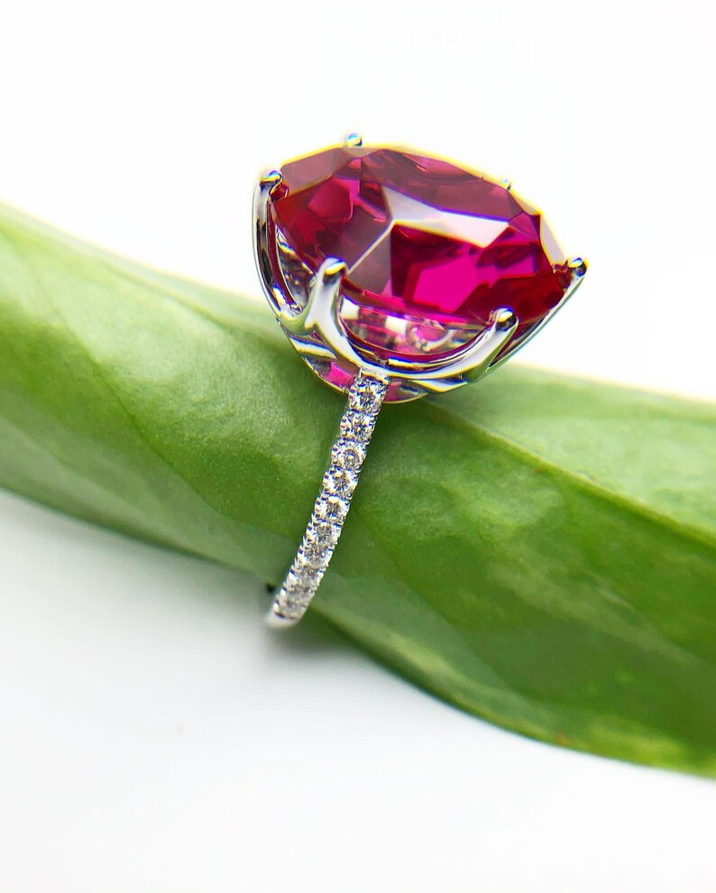 May include: A silver ring with a large, oval-shaped ruby gemstone set in a prong setting. The ring has a band of small diamonds.