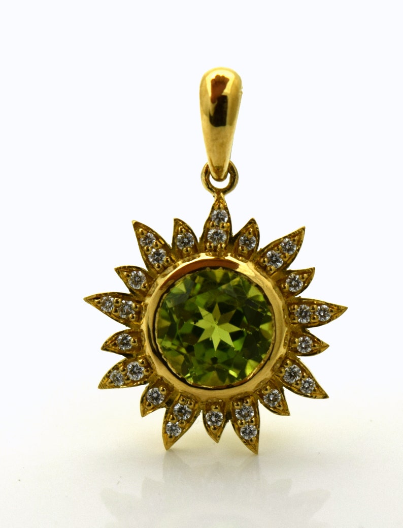 May include: A gold pendant featuring a green gemstone surrounded by a halo of small diamonds. The pendant is shaped like a sun with rays.