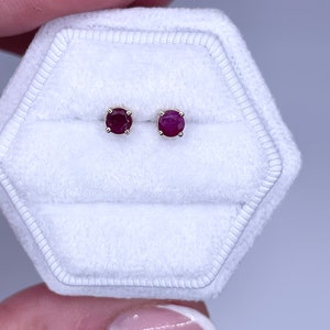 May include: A pair of ruby stud earrings in a white velvet jewellery box. The earrings are set in gold.