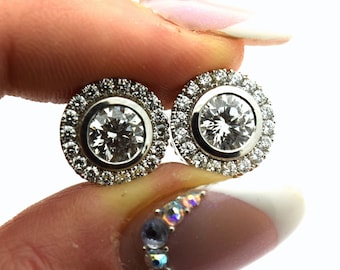 May include: A pair of silver earrings with a large round diamond center stone surrounded by a halo of smaller diamonds.