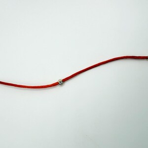 May include: A red cord bracelet featuring a single clear round stone set in a silver-toned metal bead. The bracelet includes silver-toned metal end caps, a lobster claw clasp, and a small circular jump ring at the opposite end for closure.