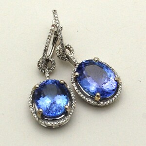 May include: A pair of silver dangle earrings with a large oval blue gemstone surrounded by a halo of smaller diamonds. The earrings have a simple, elegant design.