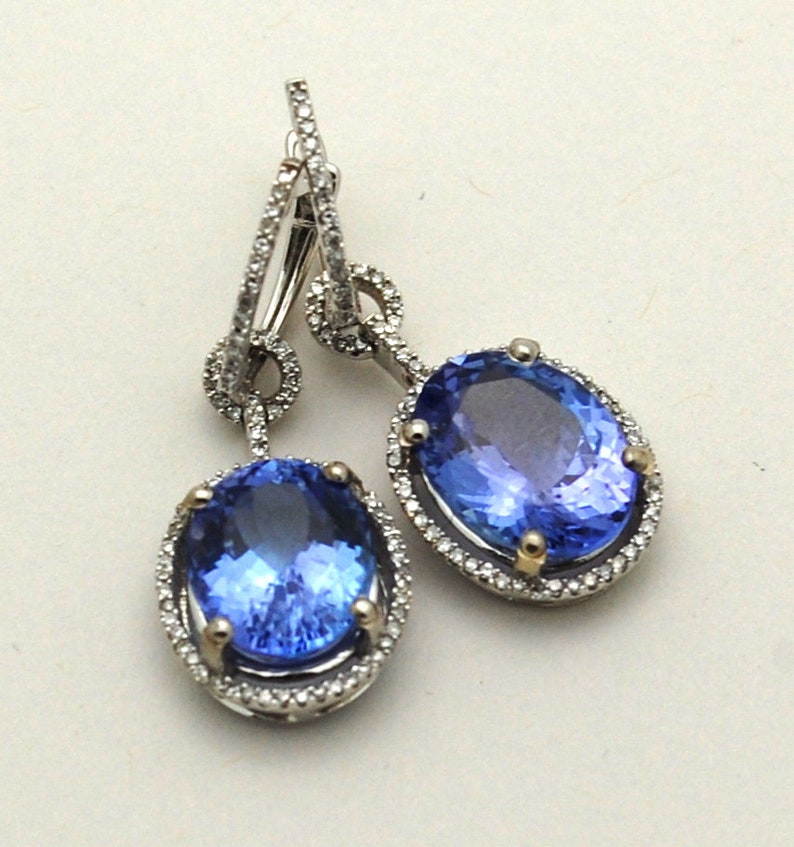 May include: A pair of silver dangle earrings with a large oval blue gemstone surrounded by a halo of smaller diamonds. The earrings have a simple, elegant design.