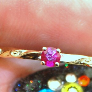 Peut inclure: Une d&eacute;licate bague en or avec une seule pierre pr&eacute;cieuse en rubis rose sertie au centre. La bague a un design ondul&eacute; et organique.