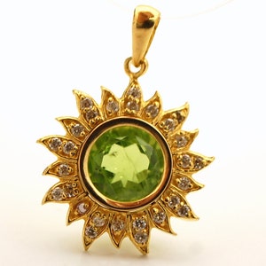 May include: A gold pendant featuring a green gemstone surrounded by a halo of small diamonds. The pendant is shaped like a sun with rays.