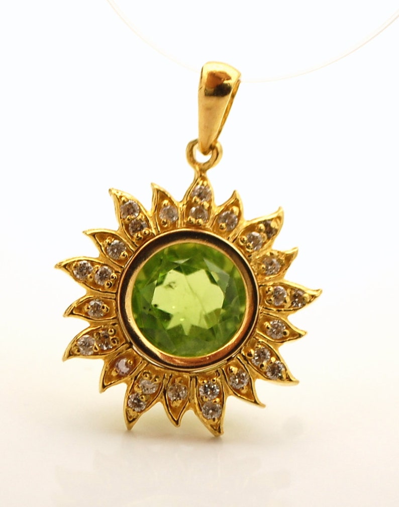 May include: A gold pendant featuring a green gemstone surrounded by a halo of small diamonds. The pendant is shaped like a sun with rays.