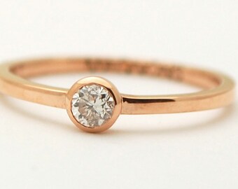 May include: A simple rose gold band ring with a single round diamond.