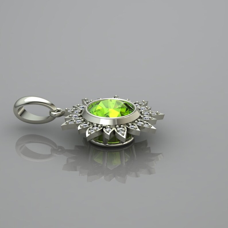 May include: A silver pendant with a green gemstone surrounded by a halo of smaller diamonds. The pendant is shaped like a sun with rays extending from the center.