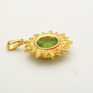 May include: A gold pendant with a green gemstone surrounded by smaller white gemstones in a sunburst design.