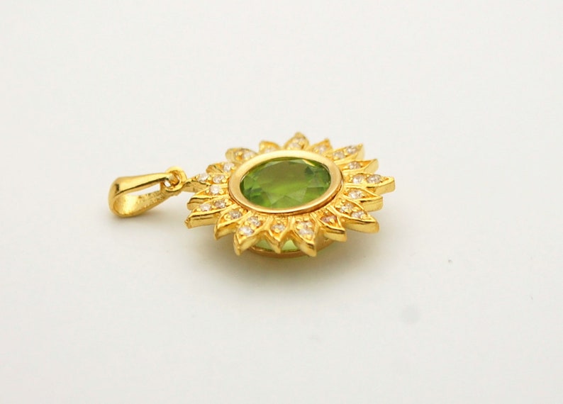 May include: A gold pendant with a green gemstone surrounded by smaller white gemstones in a sunburst design.