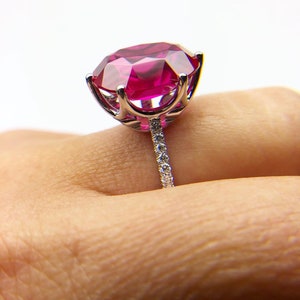 May include: A silver ring with a large, bright pink gemstone surrounded by smaller diamonds. The ring is set on a white background.