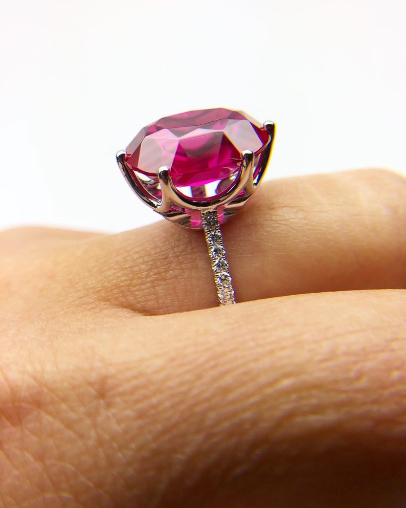 May include: A silver ring with a large, bright pink gemstone surrounded by smaller diamonds. The ring is set on a white background.