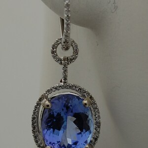 May include: A pair of silver dangle earrings with a large oval-shaped blue gemstone surrounded by a halo of small diamonds.