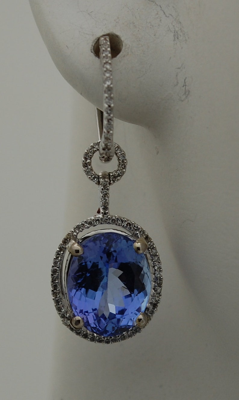 May include: A pair of silver dangle earrings with a large oval-shaped blue gemstone surrounded by a halo of small diamonds.