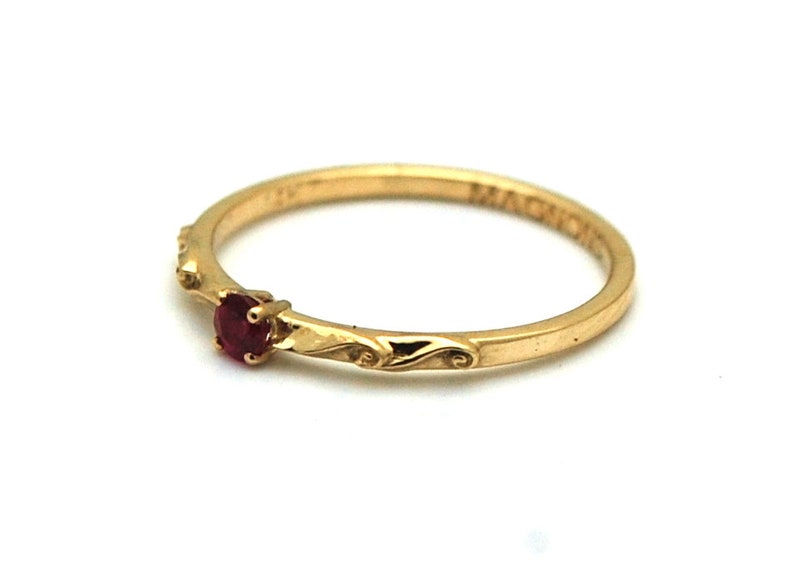 Peut inclure: Une bague en or avec une seule pierre pr&eacute;cieuse rouge et un d&eacute;licat motif floral. La bague est grav&eacute;e du mot "MAGIC".