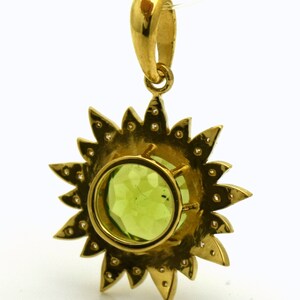 May include: A gold pendant featuring a green gemstone surrounded by a halo of smaller diamonds. The pendant is shaped like a sun with rays extending from the center.