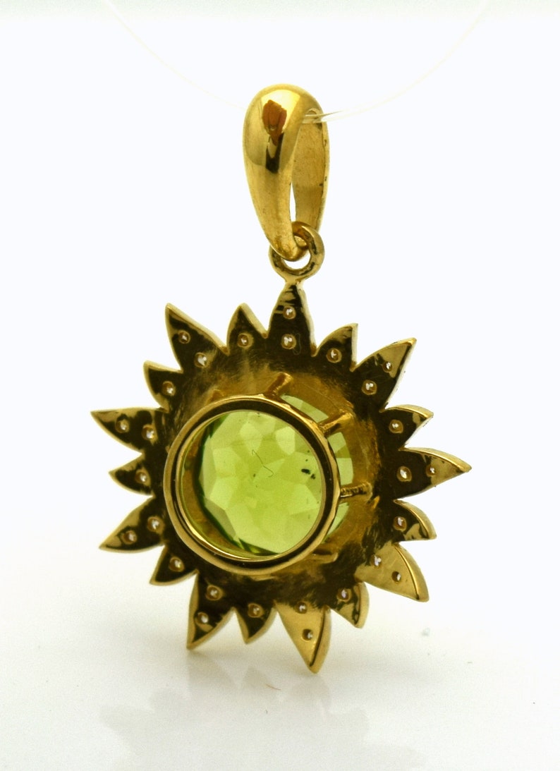 May include: A gold pendant featuring a green gemstone surrounded by a halo of smaller diamonds. The pendant is shaped like a sun with rays extending from the center.