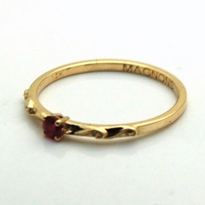 Peut inclure: Une bague en or avec une petite pierre pr&eacute;cieuse rouge et l'inscription "MAGNON" sur la bande.