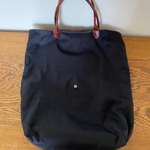 May include: A black tote bag with brown leather handles. The bag is made from durable nylon and has a simple, classic design.