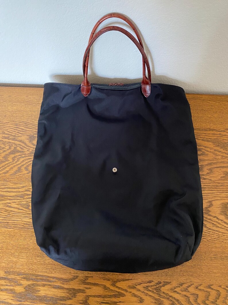 May include: A black tote bag with brown leather handles. The bag is made from durable nylon and has a simple, classic design.