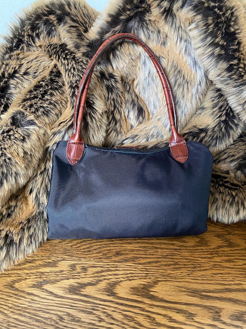 May include: A black nylon handbag with brown leather handles. The bag is resting on a wooden surface.