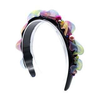 Könnte beinhalten: Ein schwarzes Stirnband mit einem farbenfrohen Blumenmuster aus Stoff. Die Blume besteht aus mehreren Schichten durchsichtigen Stoffes in den Farben Rosa, Gelb und Grün. Das Stirnband ist mit schillernden Perlen und Perlen verziert.