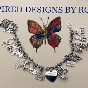 May include: A silver charm bracelet with various medical-themed charms, including a stethoscope, a syringe, a pill bottle, a car, a face mask, a ring, a building, a heart charm with the text "You're My Person", and a laptop. The bracelet is on a light brown surface with a butterfly illustration.