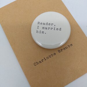 May include: White round button with the text "Reader, I married him." and the name "Charlotte Bronte" printed below the button.