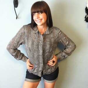 May include: A woman wearing a black and white patterned button-down shirt with a collared neckline and short sleeves. She is also wearing denim shorts.